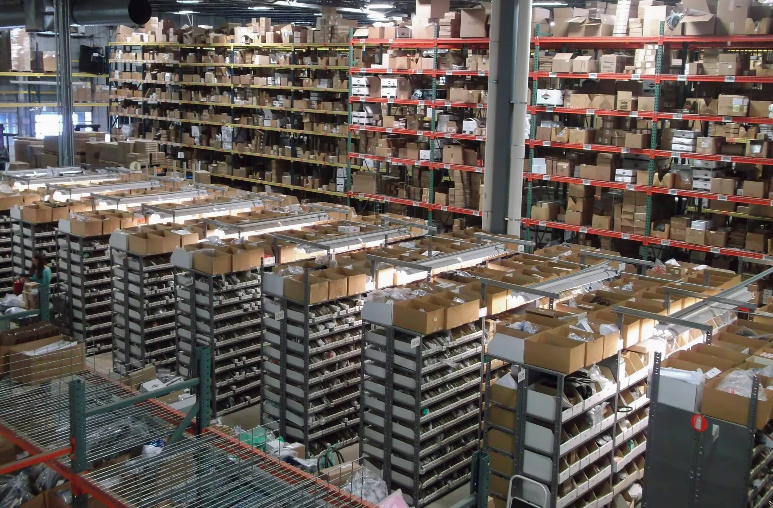 Industrial warehouse with tall metal shelves filled with cardboard boxes and bins.